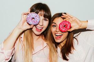 huis pyjama feest. dichtbij omhoog flash portret van twee grappig wit Dames poseren met donuts. verrassing gezicht. foto