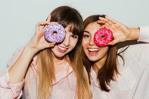 huis pyjama feest. dichtbij omhoog flash portret van twee grappig wit Dames poseren met donuts. verrassing gezicht. foto