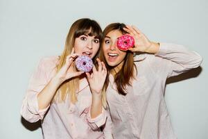 huis pyjama feest. flash portret van twee grappig Dames poseren met donuts. verrassing gezicht. foto