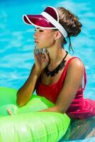 sexy gebruind vrouw in rood zwempak hebben pret en genieten van zomer in verbazingwekkend groot zwemmen zwembad. jong mooi meisje zwemmen Aan opblaasbaar ring. elegant transparant kap. strand feest. foto