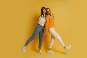 twee zussen in elegant herfst gewoontjes kleren hebben pret over- geel achtergrond in studio. vol lengte. foto