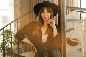 dichtbij omhoog herfst ik portret van elegant vrouw in zwart hoed en blouse poseren in Boheems interieur met trap. foto