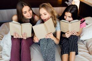 levensstijl beeld van drie het beste vrienden in pyjama lezing boeken, aan het studeren en gesprekken in slaapkamer. groep van studenten aan het doen huiswerk samen Bij huis. knus warm kleuren. emotioneel gezichten. foto