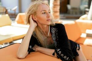 slank blond vrouw genieten vakantie , chillen in elegant strand club. vervelend elegant boho zomer kleding. foto