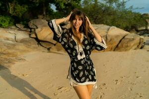 buitenshuis zomer foto van mooi brunette vrouw in boheens jurk poseren Aan tropisch strand.