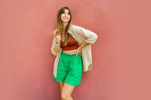 elegant vrouw in veelkleurig zomer kleding poseren over- roze achtergrond. foto