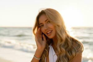 dichtbij omhoog portret van mooi blond vrouw in sexy badmode poseren Aan de strand in zonsondergang licht. prtfect golvend haren, bruinen afschuimen lichaam. zomer tropisch humeur. foto