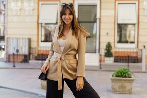 mooi brunette elegant vrouw in zonnebril en gewoontjes jasje poseren Aan de straat in mooi Europese stad. foto