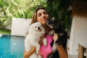 jong mooi vrouw Holding twee schattig honden, poseren in de buurt zwembad. foto