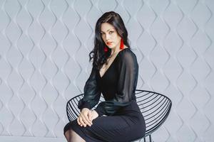 vrouw die een zwarte jurk draagt en rode oorbellen draagt, zittend op een stoel foto