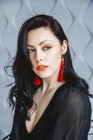vrouw draagt een zwarte jurk, rode oorbellen in lichte studio foto