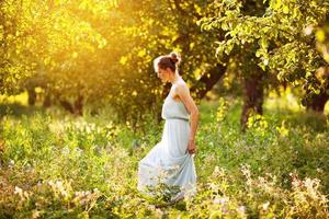 vrouw in een jurk loopt in een appelboomgaard foto