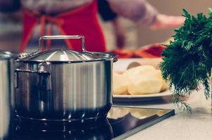 kookpot en groenten, gezonde ingrediënten voor soep of stoofpot op tafel, vrouw in de keuken op de achtergrond. zelfgemaakte gerechten, koken, vegetarisch concept foto