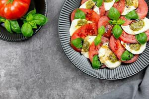 traditioneel Italiaans caprese salade met gesneden tomaten, Mozzarella, basilicum, pesto saus en kruid Aan een donker grijs beton achtergrond. top visie. kopiëren ruimte. foto