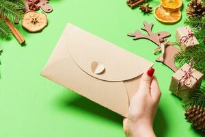 top visie van vrouw Holding een envelop Aan groen achtergrond gemaakt van vakantie decoraties. Kerstmis tijd concept foto