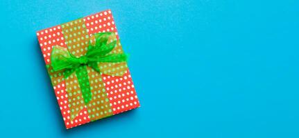 verpakt Kerstmis of andere vakantie handgemaakt Cadeau in papier met groen lint Aan blauw achtergrond. Cadeau doos, decoratie van geschenk Aan gekleurde tafel, top visie met kopiëren ruimte foto