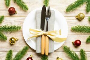 top visie van nieuw jaar avondeten Aan feestelijk houten achtergrond. samenstelling van bord, vork, mes, Spar boom en decoraties. vrolijk Kerstmis concept foto