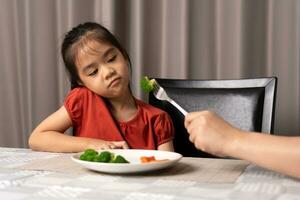 weinig schattig kind meisje weigeren naar eten gezond groenten. kinderen Doen niet Leuk vinden naar eten groenten. foto