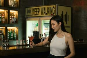 Aziatische vrouw die 's nachts een cocktail drinkt in een bar. foto