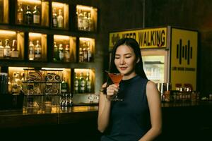 Aziatische vrouw die 's nachts een cocktail drinkt in een bar. foto