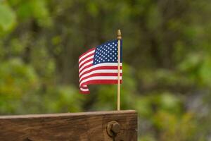 deze is een beeld van een klein Amerikaans vlag vastgemaakt naar een houten straal. deze patriottisch Scherm looks katern kleurrijk met de rood, wit, en blauw. de symbool van Amerikaans is voorzichtig vloeiende in de wind. foto