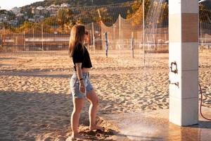 een meisje in korte broek en een zwart t-shirt op het strand bij de douche. foto