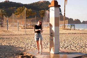 een meisje in korte broek en een zwart t-shirt op het strand bij de douche. foto