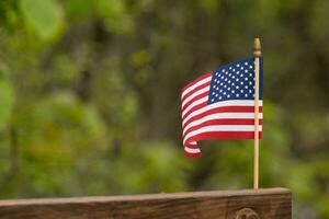 deze is een beeld van een klein Amerikaans vlag vastgemaakt naar een houten straal. deze patriottisch Scherm looks katern kleurrijk met de rood, wit, en blauw. de symbool van Amerikaans is voorzichtig vloeiende in de wind. foto