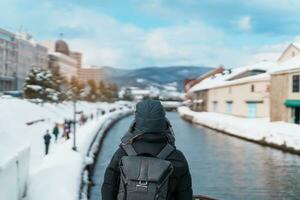 Mens toerist bezoekende in otaru, gelukkig reiziger in trui bezienswaardigheden bekijken Otaru kanaal met sneeuw in winter seizoen. mijlpaal en populair voor attracties in hokkaido, Japan. reizen en vakantie concept foto