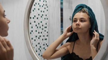 vrouw met een handdoek kijkt in de spiegel in de badkamer foto