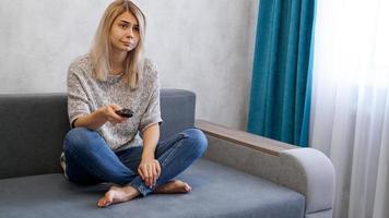 jonge vrouw verandert tv-zenders met afstandsbediening zittend op de bank
