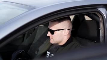 zijaanzicht van zelfverzekerde jonge stijlvolle man in zonnebril in zijn auto