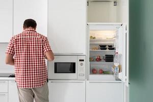 jonge man makind thee staat naast de open koelkast. foto