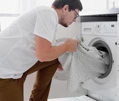 jonge man die kleren in de wasmachine stopt foto