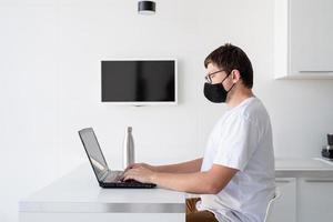 jonge man met een zwart beschermend masker die vanuit huis met een laptop werkt