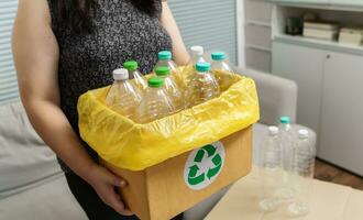 huis recycle eco groen nul concept vrouw het werpen leeg plastic fles in recycling bak met geel vuilnis Tassen Bij huis. foto