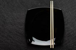 leeg zwart bord met eetstokjes Aan donker achtergrond. Japans voedsel stijl. top visie met kopiëren ruimte foto