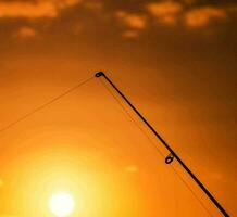 een visvangst hengel is aftekenen tegen de instelling zon foto