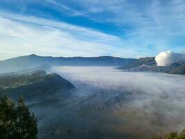 de Doorzichtig lucht is mooi en blauw met monteren bromo nog steeds emitting vulkanisch rook kant door kant met monteren batok. de zee van zand vlaktes begon naar verschijnen omdat de mist begon naar verdwijnen langzaam foto