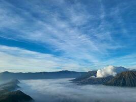 de Doorzichtig lucht is mooi en blauw met monteren bromo nog steeds emitting vulkanisch rook kant door kant met monteren batok. de zee van zand vlaktes begon naar verschijnen omdat de mist begon naar verdwijnen langzaam foto