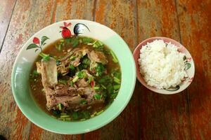 varkensvlees ruggegraat pittig soep of Tom lengte in keramisch kom en rijst- kom Aan oud bruin hout tafel. zacht, verzuren en heet soep favoriete menu in Thailand. foto