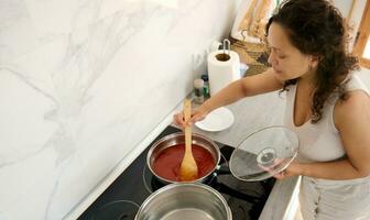 overhead visie charmant Italiaans vrouw staand door elektrisch fornuis, menging ingrediënten in een frituren pan terwijl Koken avondeten foto