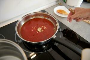 visie van bovenstaand van een pan met tomaat saus en gehakt knoflook, Aan de elektrisch fornuis in de huis keuken. detailopname foto