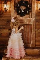 klein meisje in roze jurk staat voor houten deur