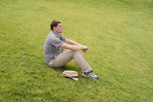 jonge nadenkende man zittend op het gras in het park