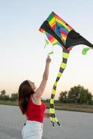 jonge vrouw die een vlieger vliegt in een openbaar park bij zonsondergang foto