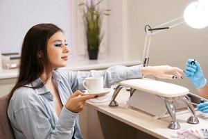 vrouw krijgt manicure in salon en houdt witte kop koffie vast foto
