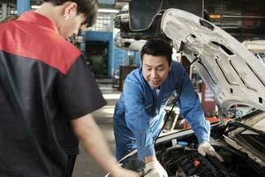 Aziatisch mannetje professioneel automotive ingenieur leidinggevende beschrijft auto motor onderhoud en reparatie werk met monteur arbeider personeel team in fix onderhoud garage, specialist beroepen in auto industrie. foto