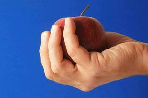 een hand- Holding een appel tegen een blauw achtergrond foto