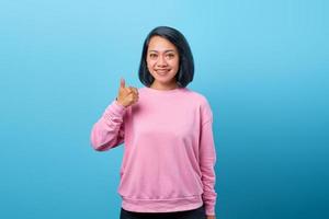 lachende Aziatische vrouw duimen opdagen op blauwe achtergrond foto
